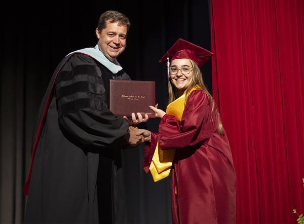 Dr. Gilliam and Ashley each hold one side of a diploma while shaking hands. They smile to camera.